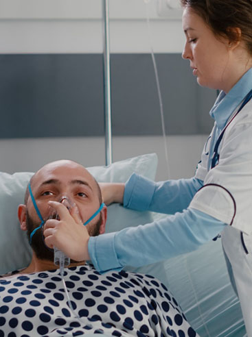 A healthcare professional in a white coat attends to a patient lying on a hospital bed wearing a polka dot gown.