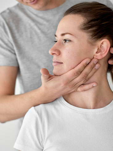 A person in a gray shirt gently applies pressure to another person's neck, indicating a massage or therapeutic technique.